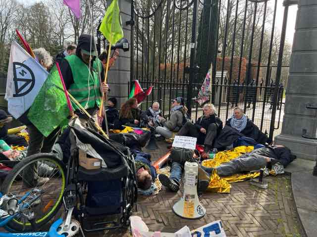 Rebels with XR flags stand and sit in front of the entrance gate of Huis ten Bosch Palace during the swearing-in of the Jetten cabinet. Some rebels are wearing keffiyehs, and a Palestinian flag hangs from the entrance gate.